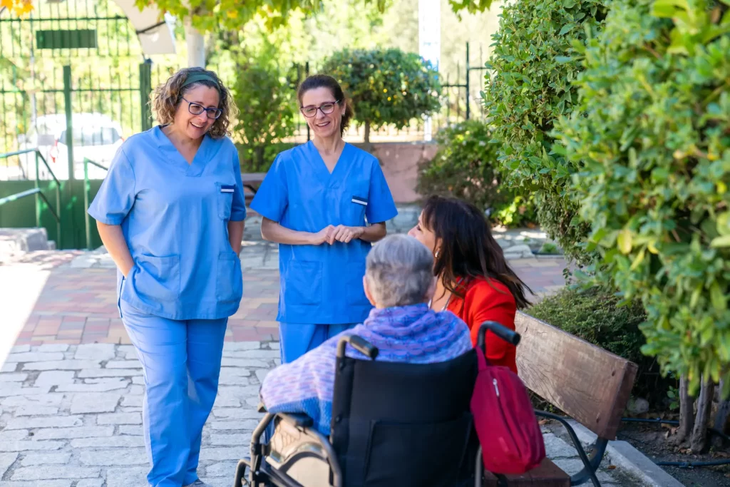 three hospice nurses talking to a hospice patient in wheel chair.