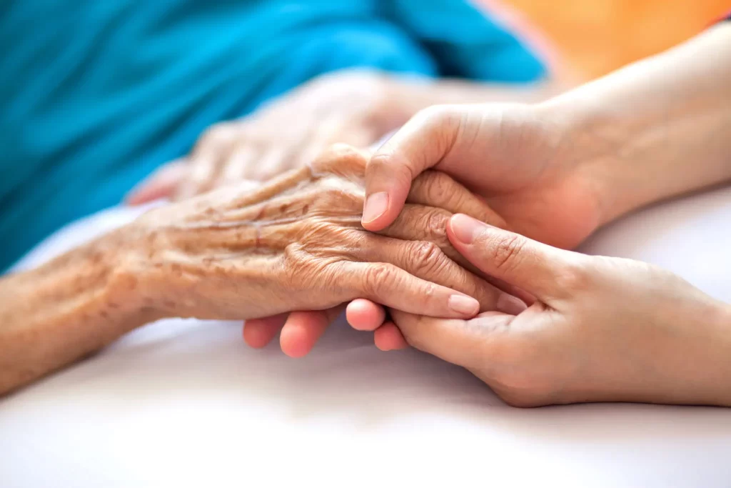 Hospice nurse holding a dying patient's hands compassionate