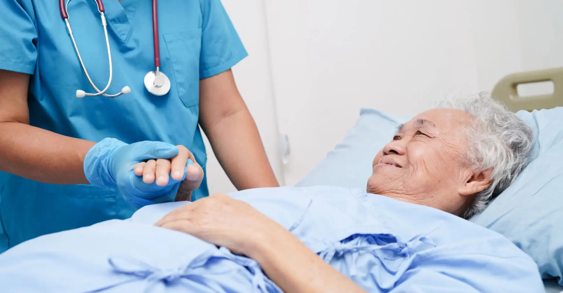 a hospice nurse compassionately holding a dying hospice patient's hands.